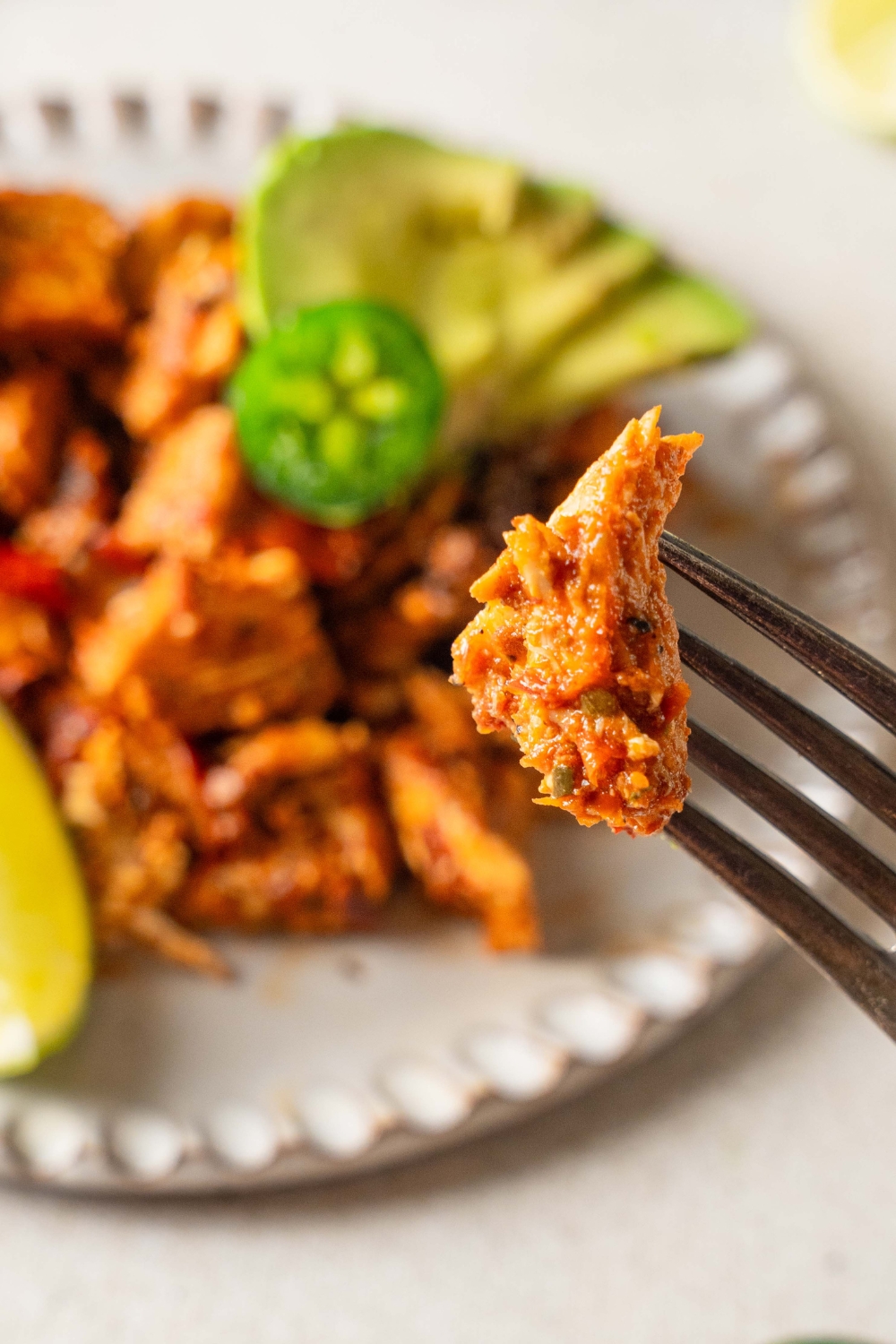 A fork with a piece of chicken al pastor with a plate of the remaining chicken al pastor in the background.