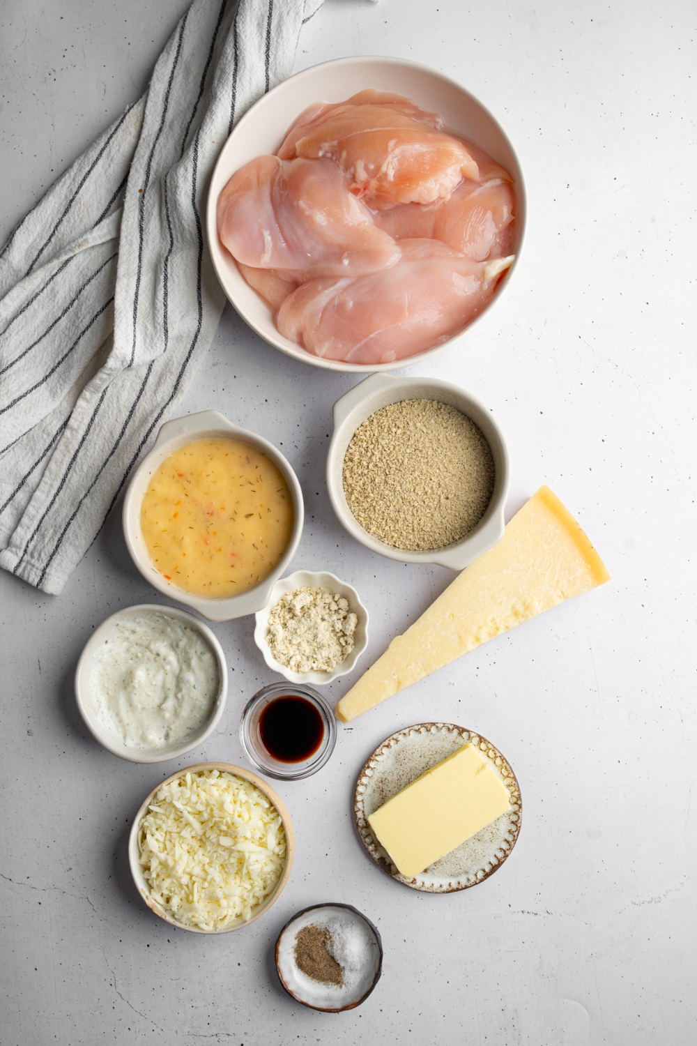 An overhead shot of several bowls in various sizes containing ingredients to make copycat Longhorn parmesan crusted chicken including chicken breasts, italian dressing, ranch dressing, provolone cheese, panko breadcrumbs, and seasonings.