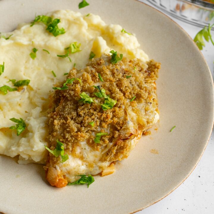 Copycat Longhorn parmesan crusted chicken served with mashed potatoes garnished with fresh parsley. The plate is on a white counter with a white striped napkin.