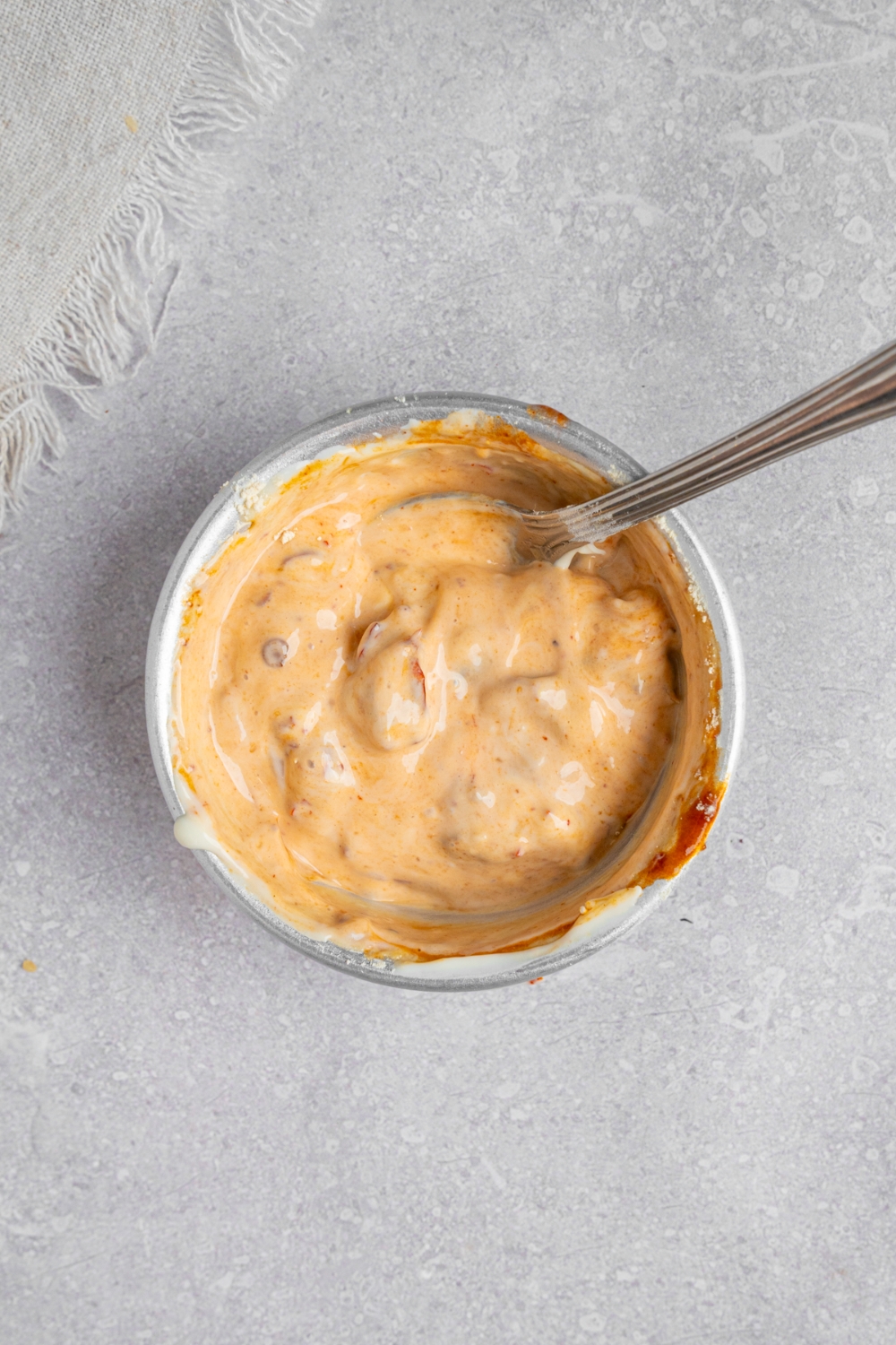 A spoon mixing chipotle mayo in a small white bowl. The bowl is on a white counter with a white cloth napkin.