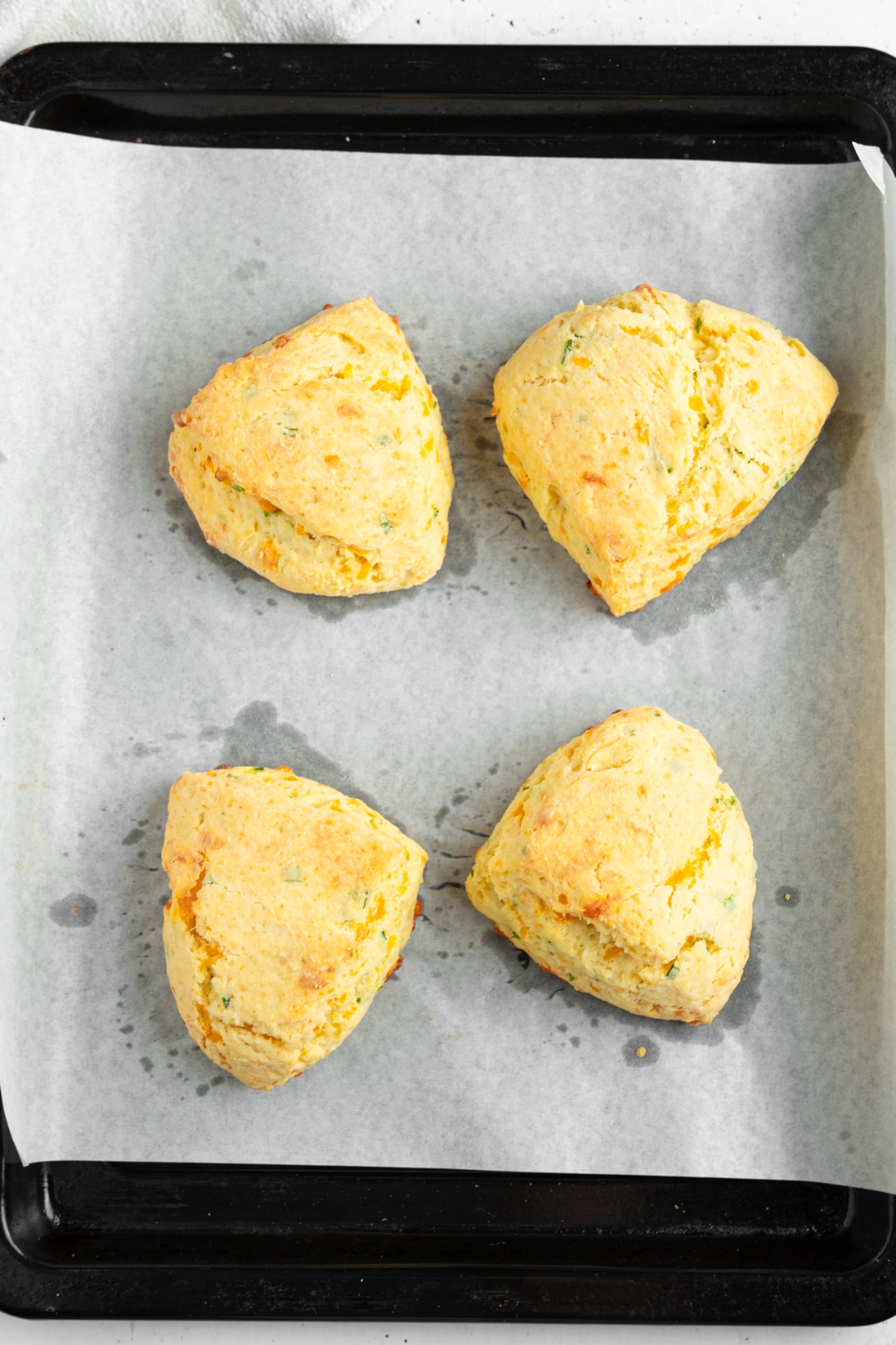 A baking sheet lined with parchment paper with four baked cheddar chive savory scones.