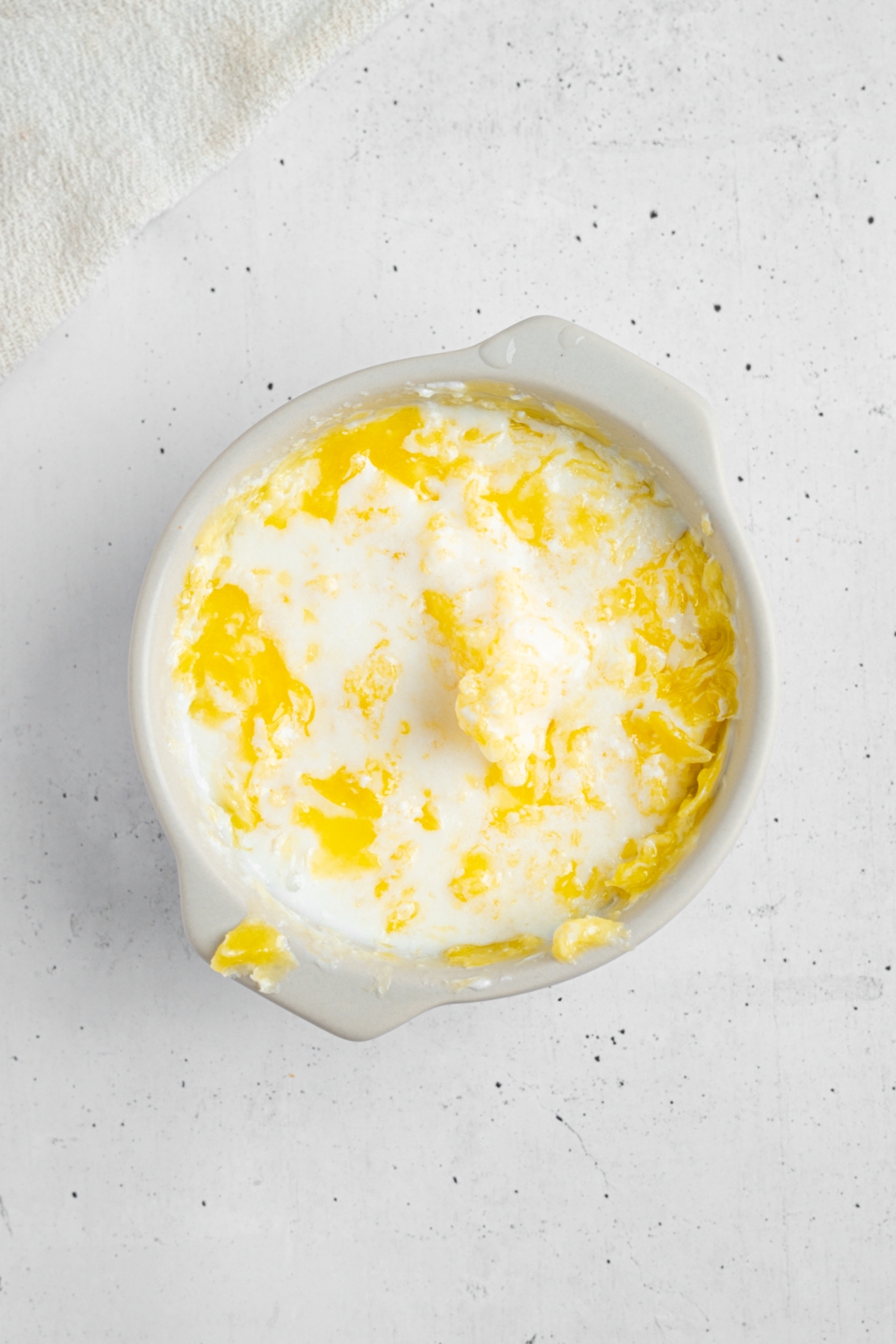 A ceramic bowl of cheddar chive biscuit dry ingredients mixed with buttermilk. The bowl is on a white counter.