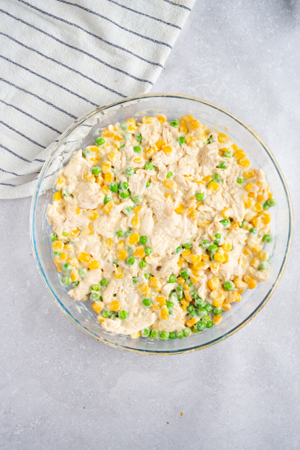 A round glass baking dish with rotisserie chicken casserole filling. The dish is on a white counter with a white striped napkin.
