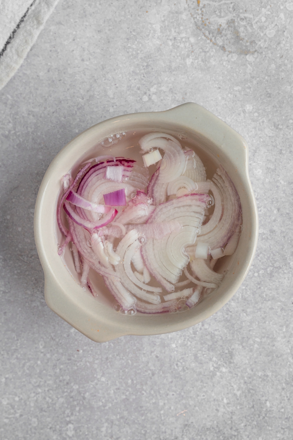 A ceramic bowl with red onions pickling in vinegar. The bowl is on a white counter.