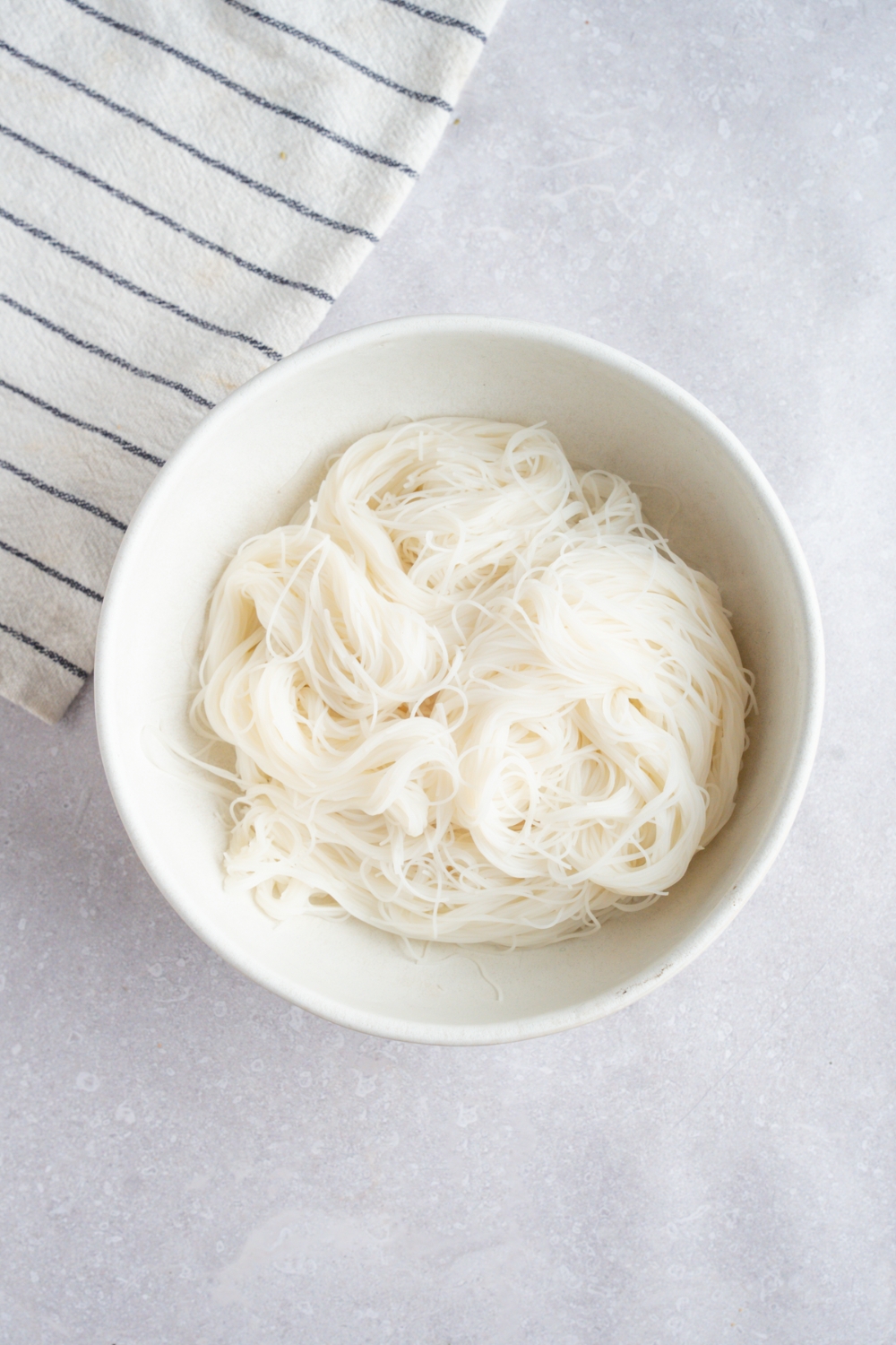 A white bowl with cooked pho noodles. The bowl is on a white counter with a white striped napkin.