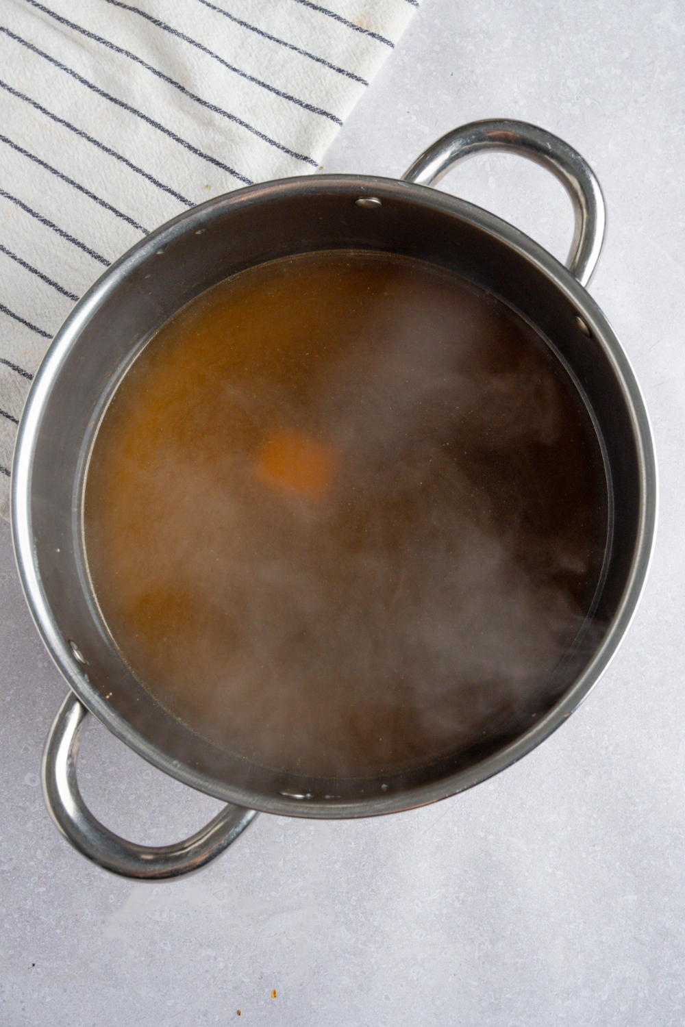 A stock pot with cooked rotisserie chicken pho broth. The pot is on a white counter with a white striped napkin.
