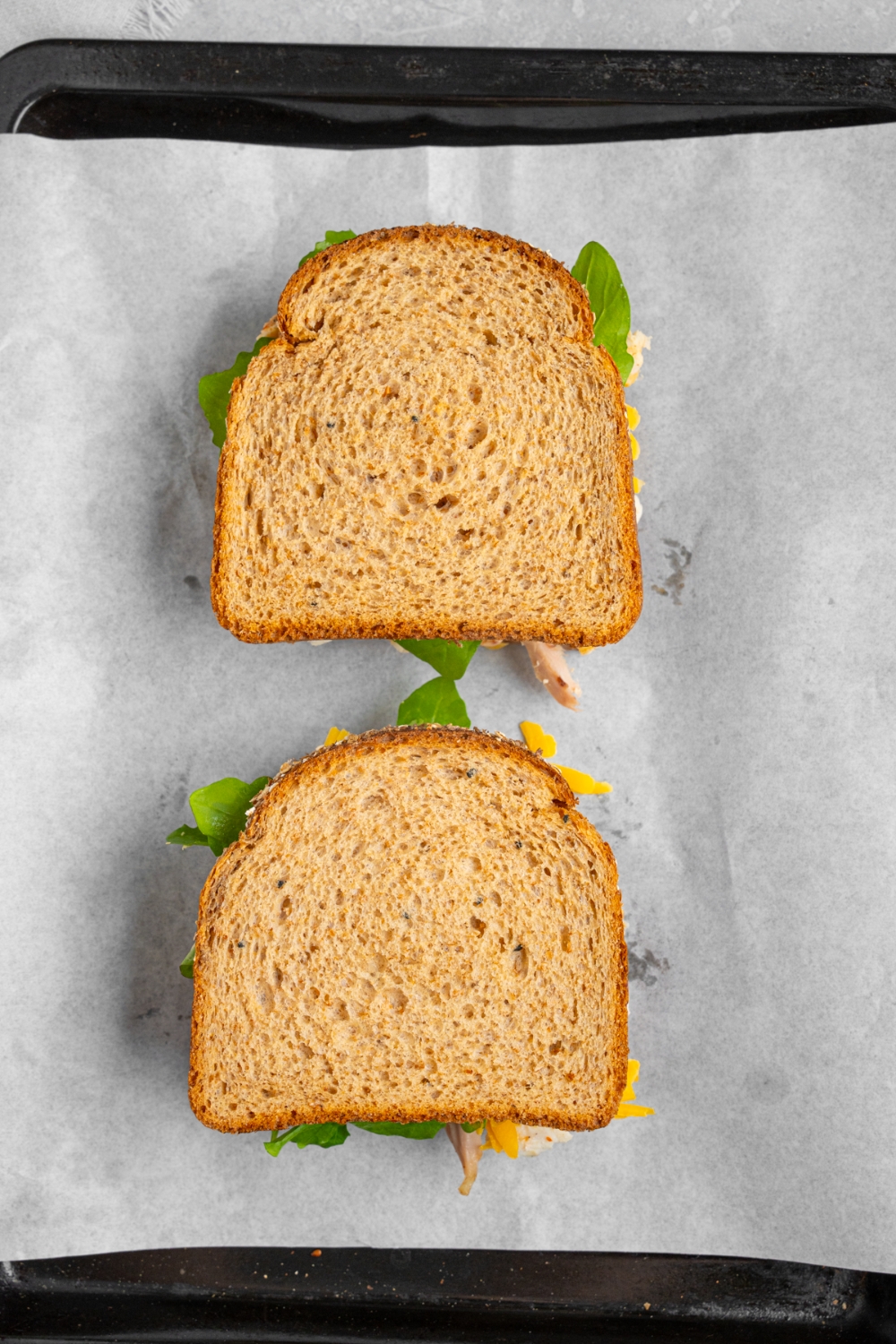 A baking sheet lined with parchment paper with two whole unbaked rotisserie chicken sandwiches.