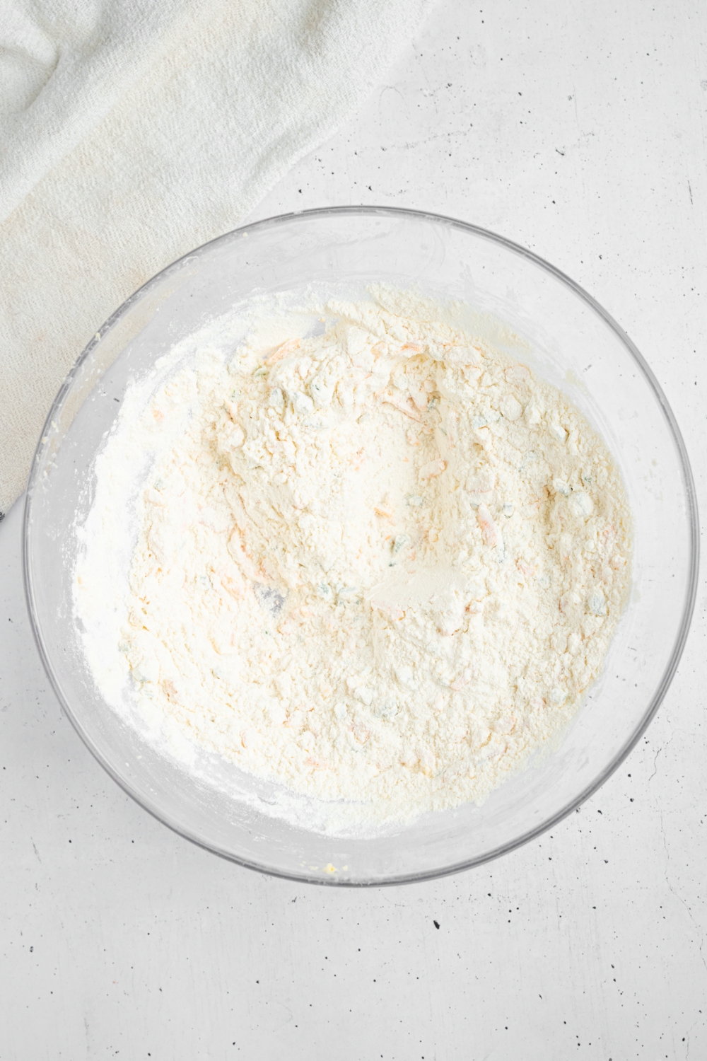 A glass bowl with dry ingredients for cheddar chive scones including flour, sugar, baking powder, and salt.