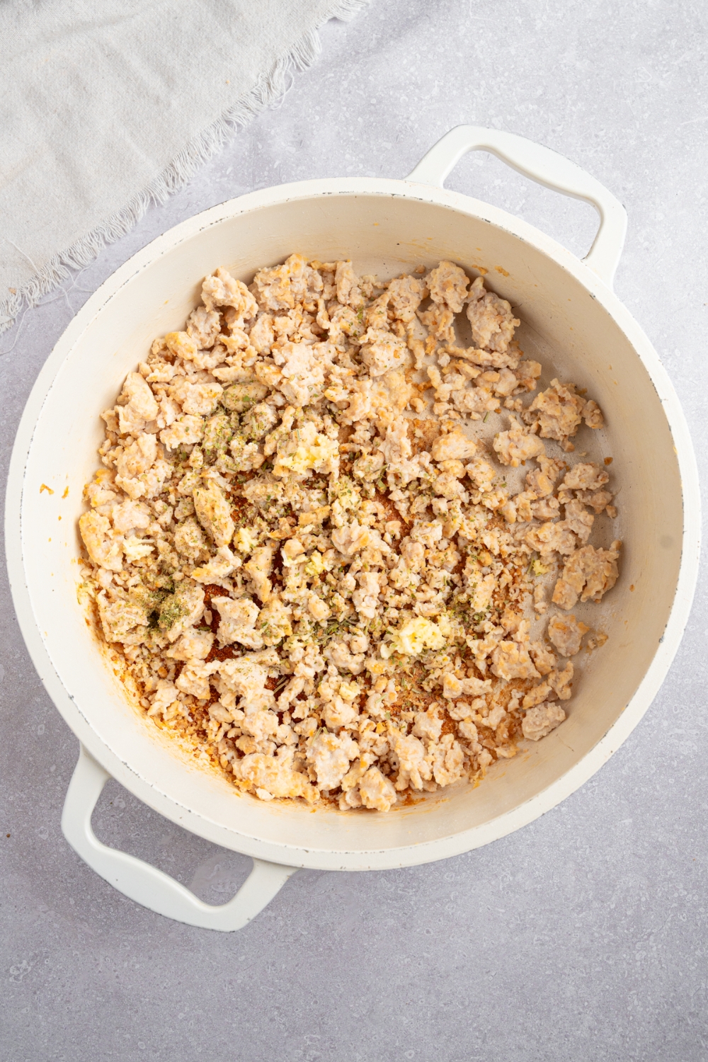 A large white pot with ground chicken cooked with seasonings. The pot is on a white counter with a white cloth napkin.