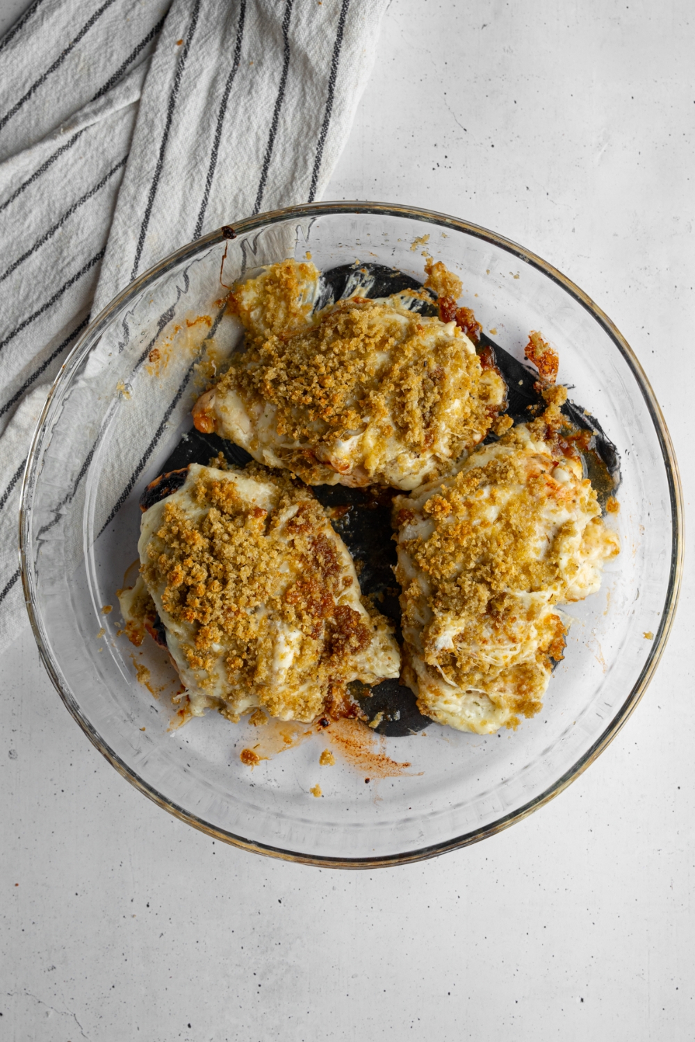 A glass baking dish with three pieces of copycat Longhorn parmesan crusted chicken. The dish is on a white counter with a white striped napkin.