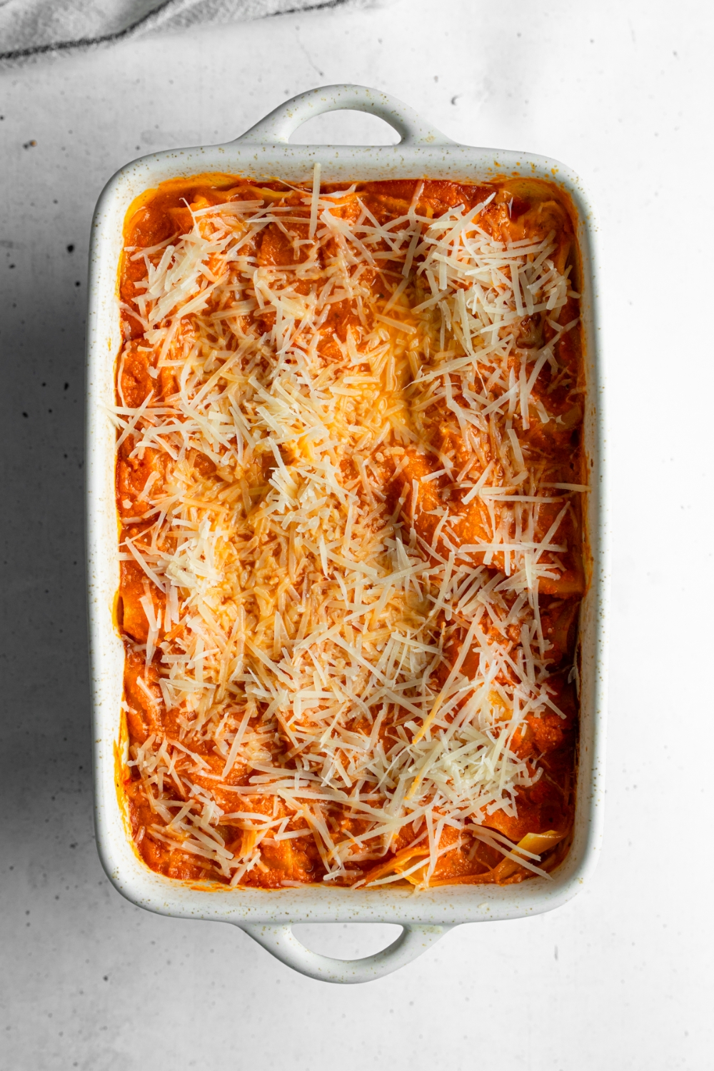 A baking dish with rotisserie chicken lasagna topped with shredded mozzarella cheese. The dish is on a white counter.