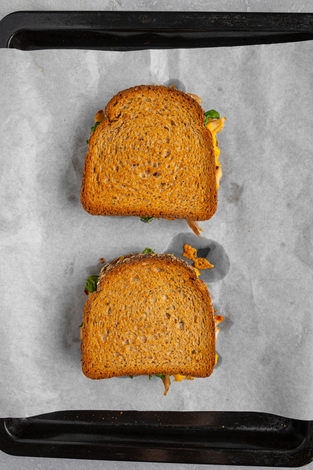 A baking sheet lined with parchment paper with two whole toasted rotisserie chicken sandwiches.