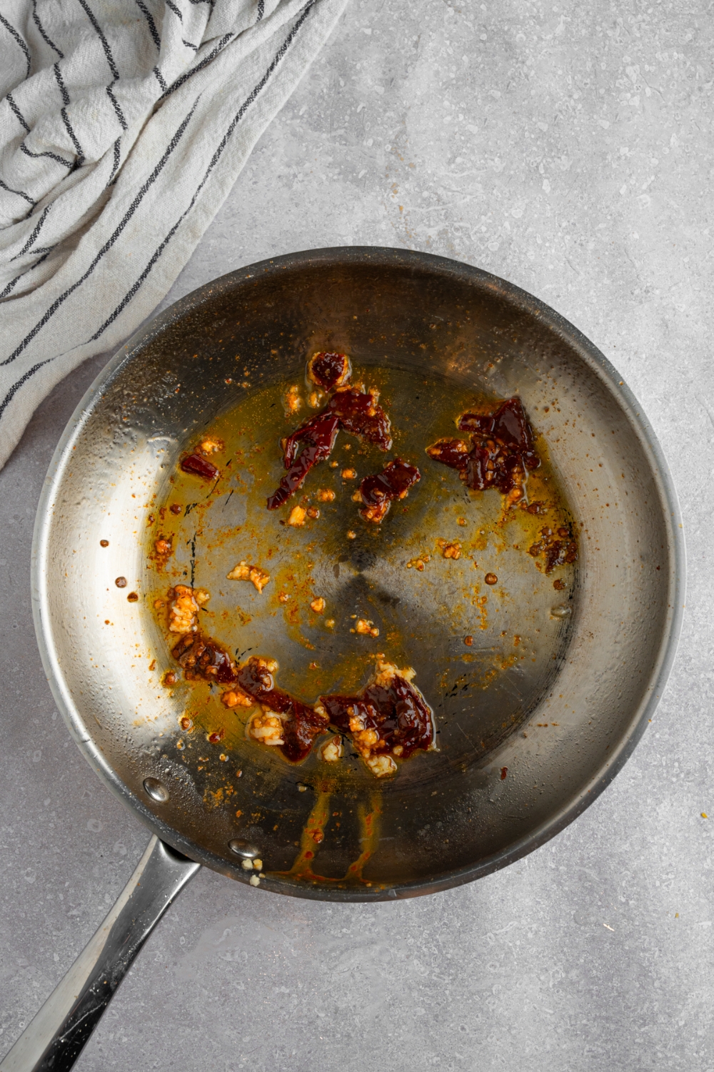 A skillet with chipotle chiles and garlic sauteing in oil. The skillet is on a white counter with a white striped napkin.