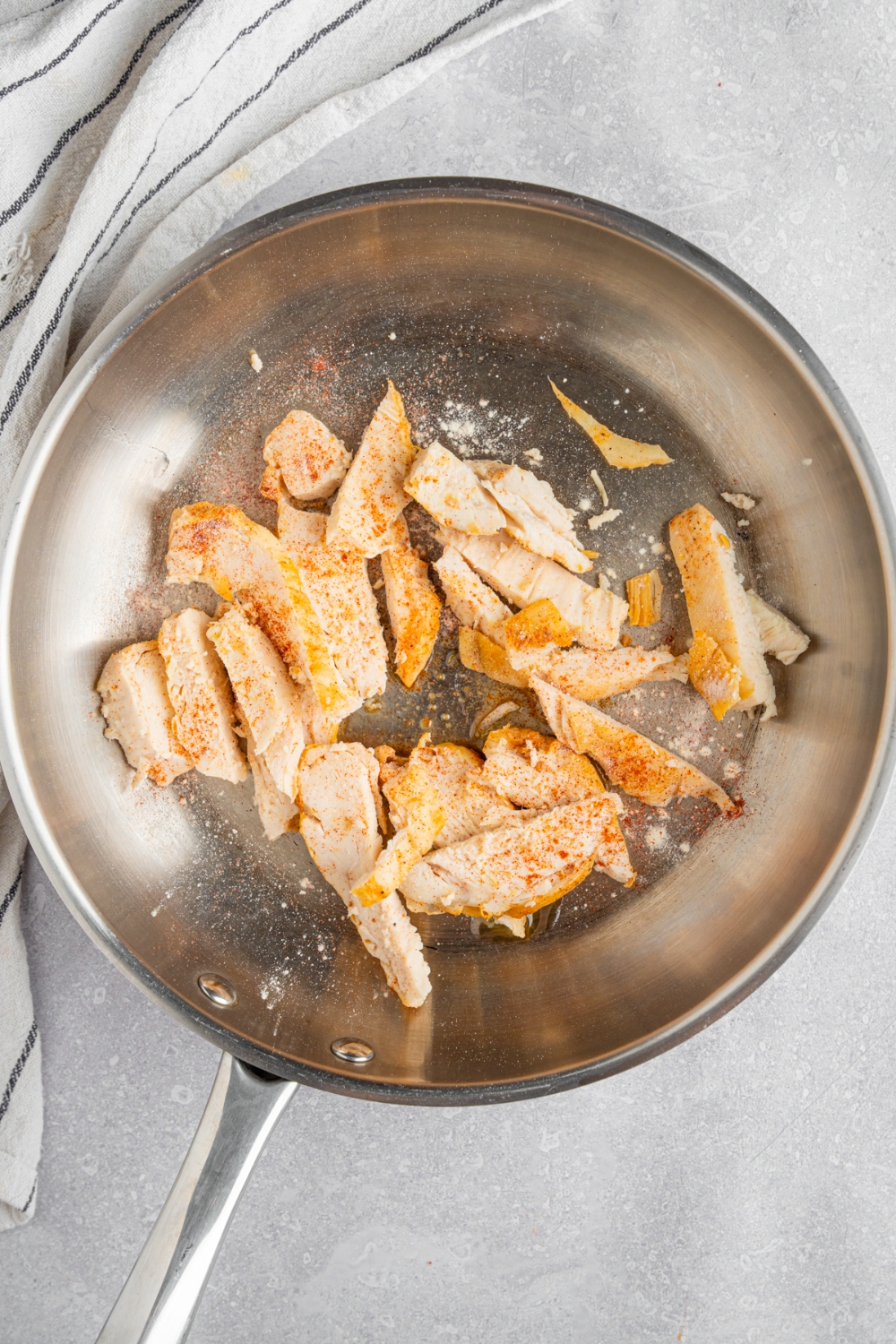 A skillet with shredded chicken on a white counter with a white striped napkin.