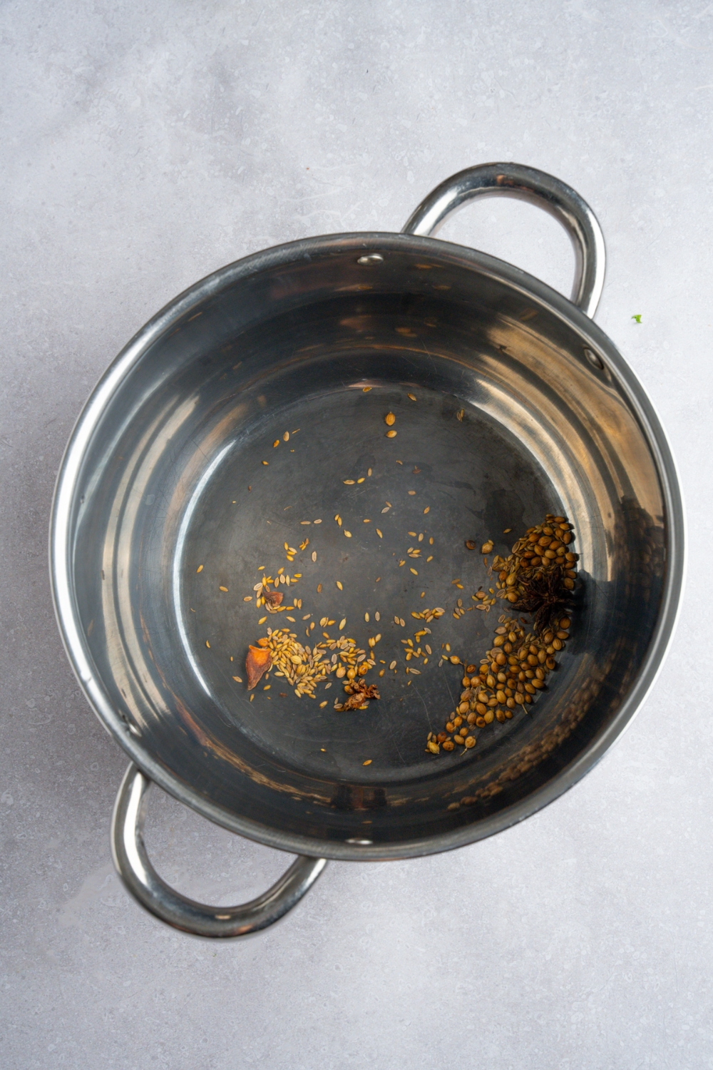 A stock pot with rotisserie chicken pho spices including star anise, coriander seed, fennel seed, and black peppercorn. The pot is on a white counter.