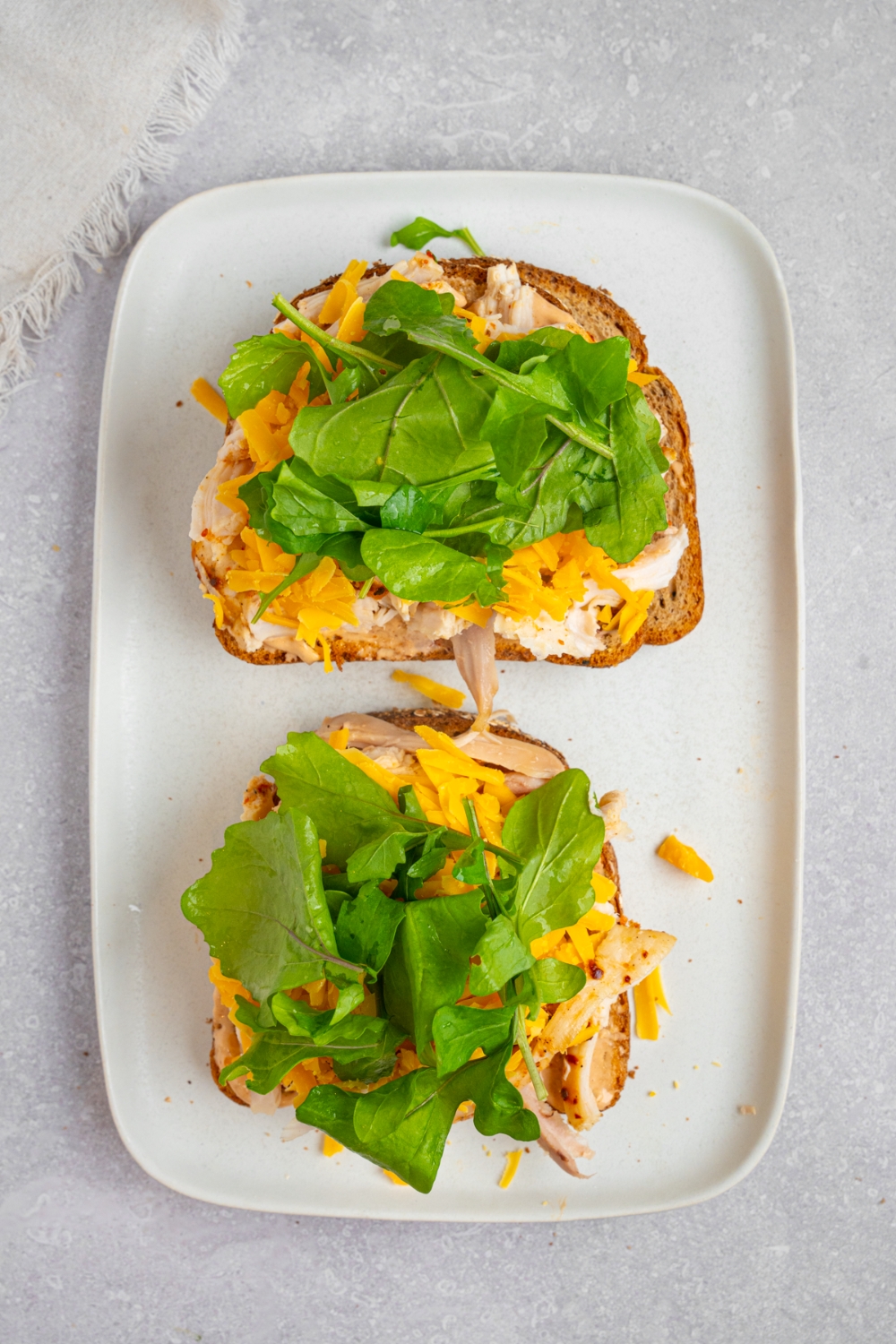 A white plate with an open rotisserie chicken sandwich with chipotle mayo, cheese, and spinach. The plate is on a white counter.