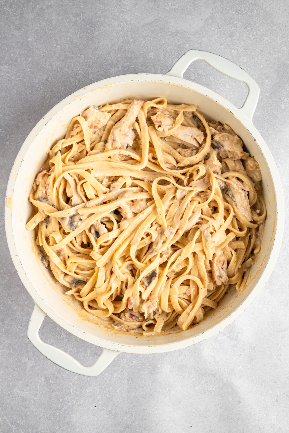A dutch oven with rotisserie chicken stroganoff tossed together. The dish is on a white counter.