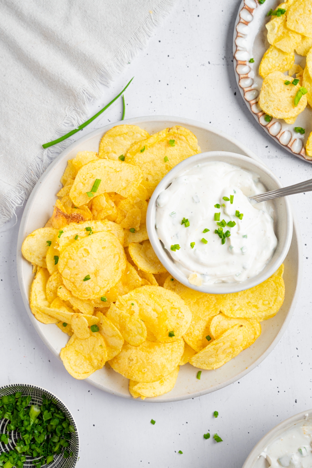 A bowl of sour cream and chive dip on a white plate with potato chips.