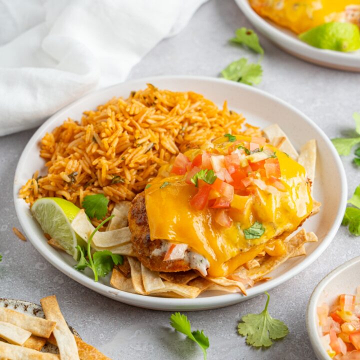 Homemade Applebee's fiesta lime chicken topped with pico de gallo and fresh cilantro. The chicken is on a white plate with Mexican rice. The plate is on a white counter with chips and an additional plate of chicken.