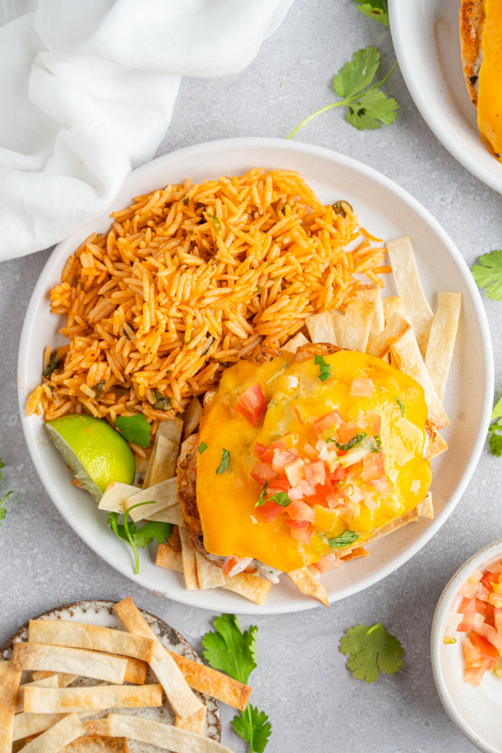 Homemade Applebee's fiesta lime chicken topped with pico de gallo and fresh cilantro. The chicken is on a white plate with Mexican rice. The plate is on a white counter with chips.