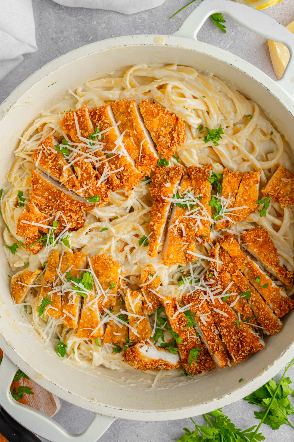 A dutch oven with homemade Olive Garden chicken fritta garnished with fresh parsley and cheese. The oven is on a white counter.