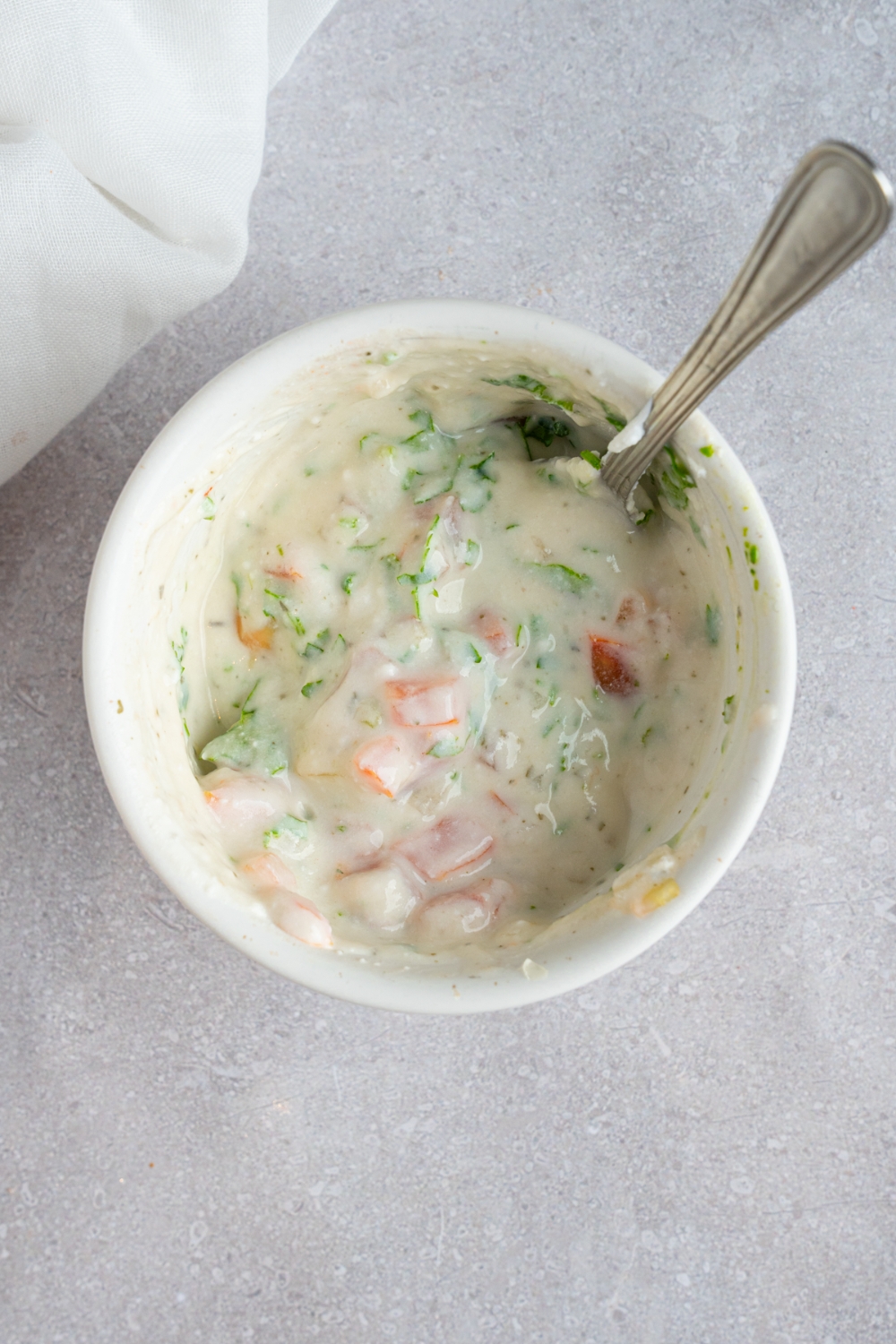 A small bowl with a spoon stirring a fiesta lime sauce. The bowl is on a white counter with a white cloth napkin.
