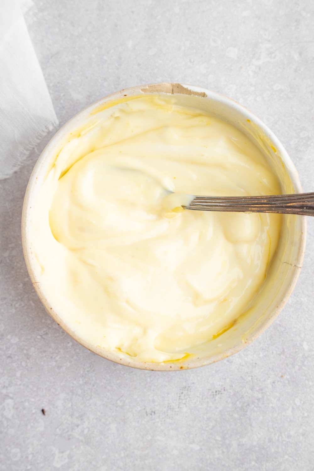 A bowl with a spoon mixing a homemade McDonald's chicken sandwich sauce. The bowl is on a white counter.