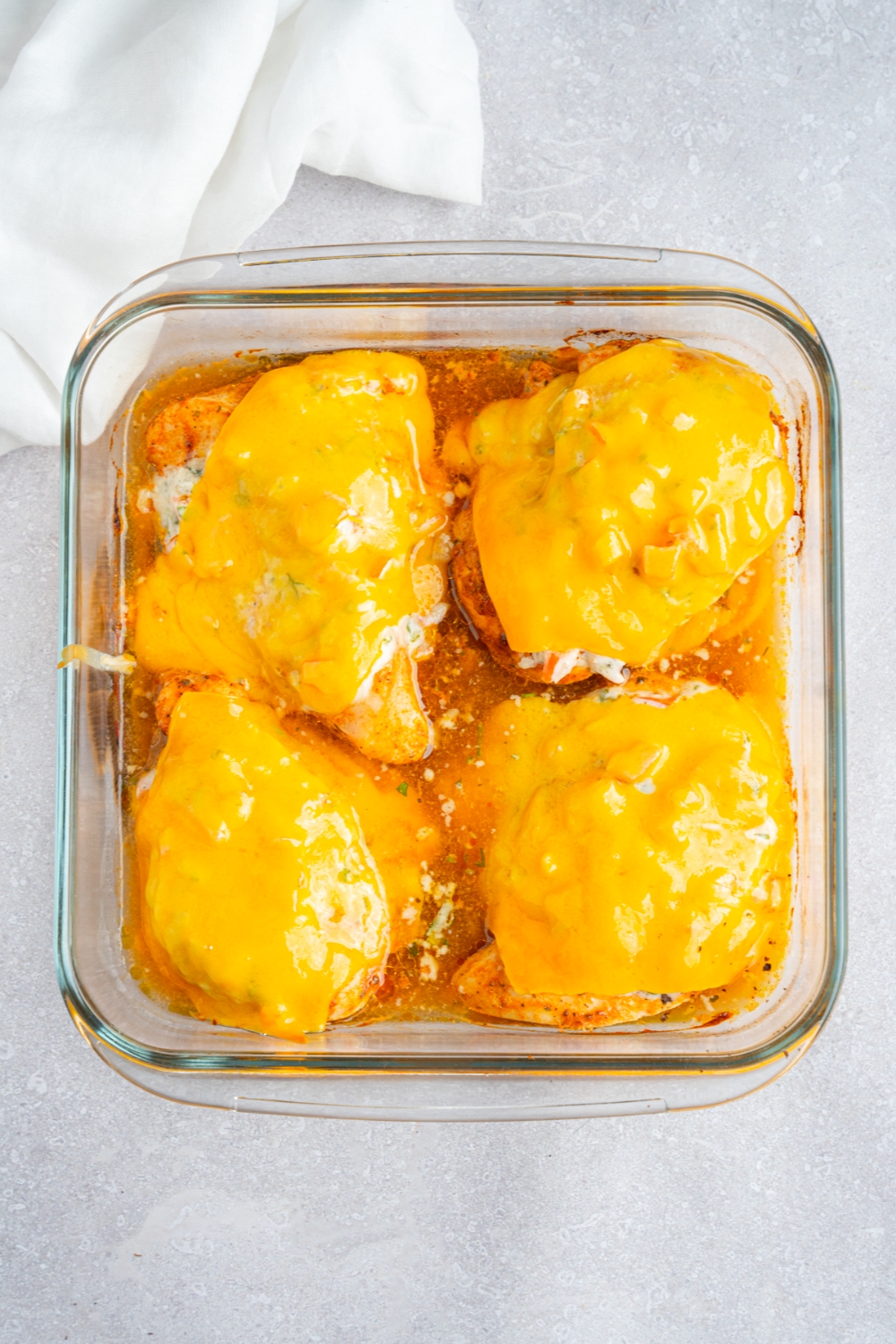 A glass baking dish with four pieces of baked chicken breasts topped with a fiesta lime sauce and sliced cheese. The dish is on a white counter with a white cloth napkin.