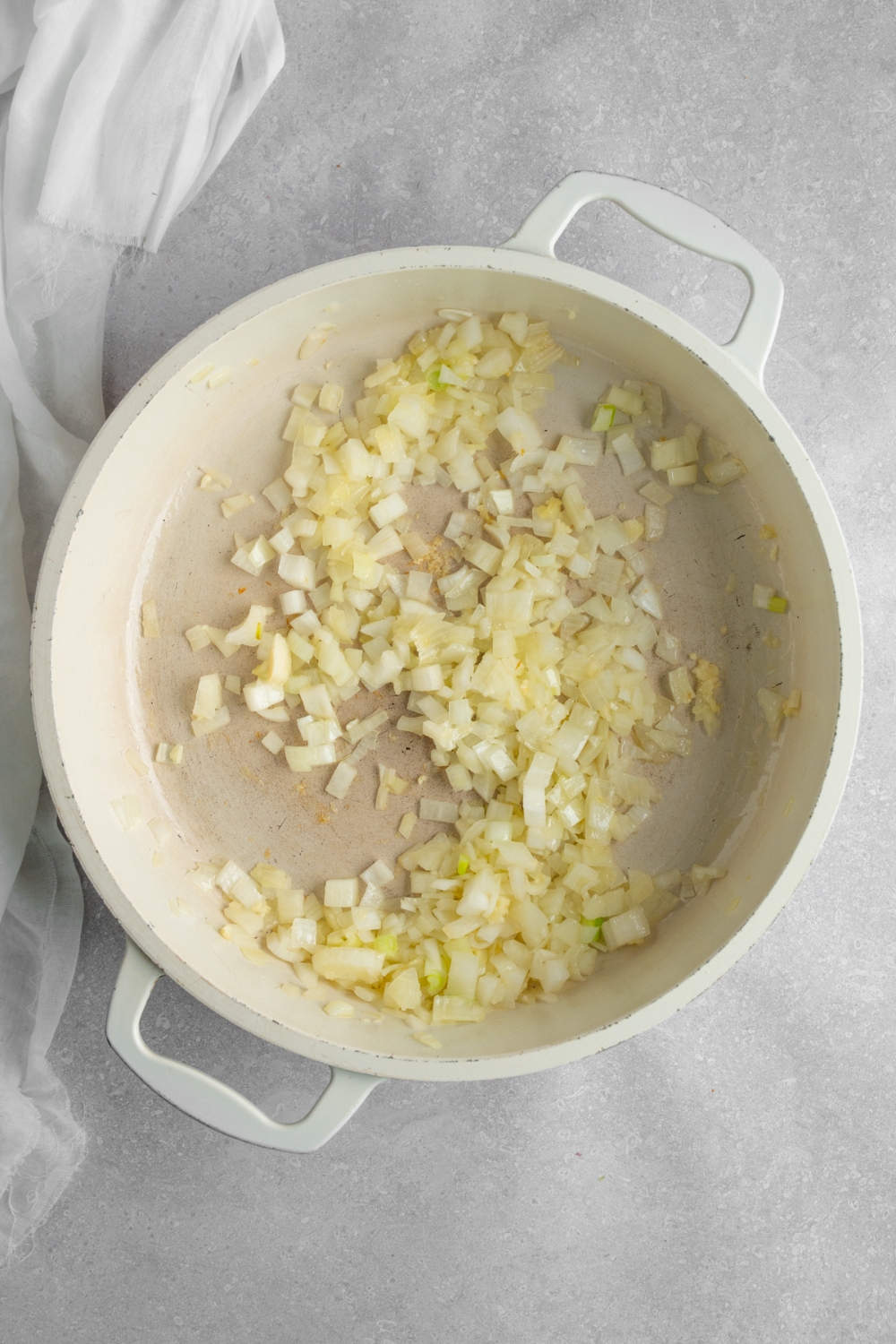 A stock pot with sauteed diced onion. The pot is on a white counter with a white napkin.