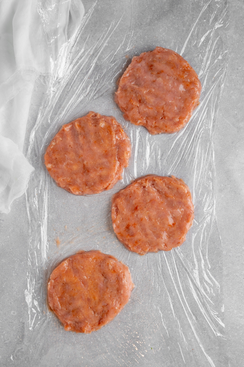 Four chicken patties on saran wrap on a white counter.