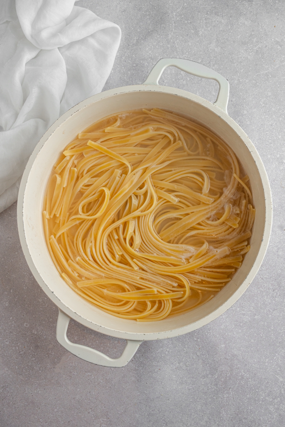 A dutch oven fettuccine pasta cooking in water. The dutch oven is on a white counter with a white napkin.