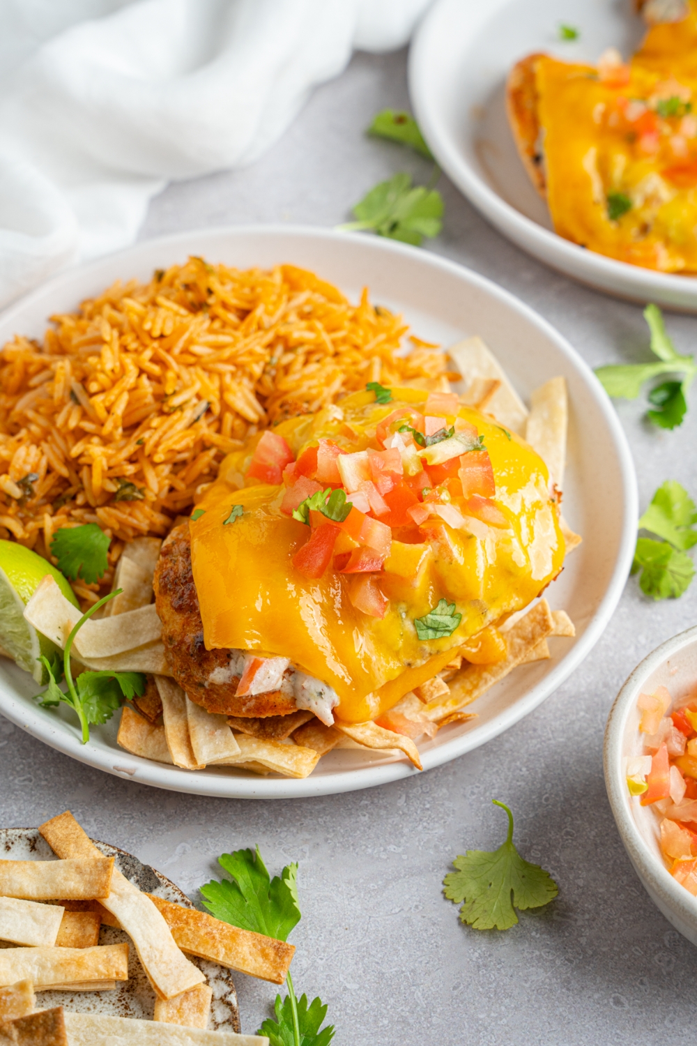 Homemade Applebee's fiesta lime chicken topped with pico de gallo and fresh cilantro. The chicken is on a white plate with Mexican rice. The plate is on a white counter with chips and an additional plate of chicken.