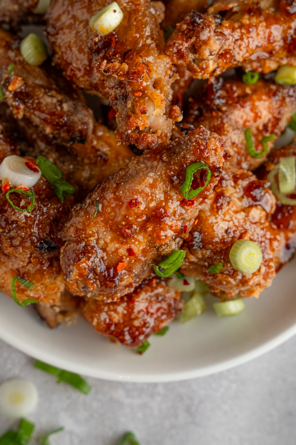 A bowl of fish sauce chicken wings garnished with sliced green onion. The bowl is on a white counter.