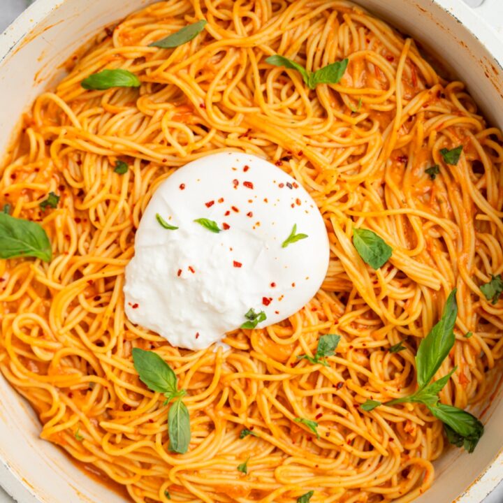 A ceramic pot of burrata spaghetti garnished with fresh basil. The pot is on a white counter with fresh basil.