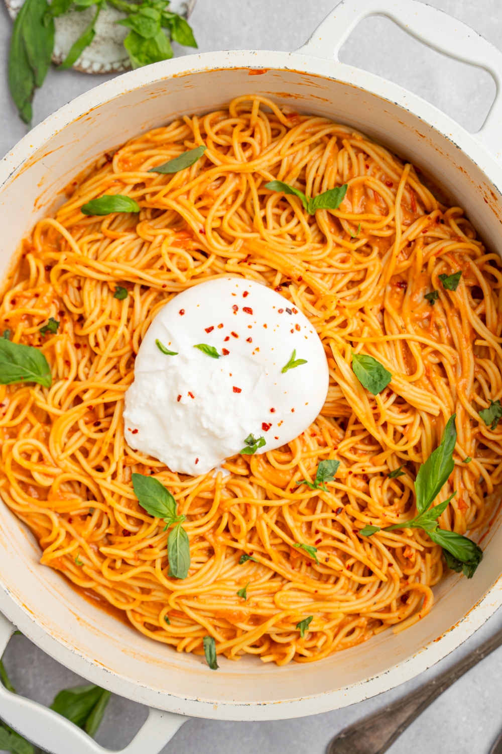 A ceramic pot of burrata spaghetti garnished with fresh basil. The pot is on a white counter with fresh basil.