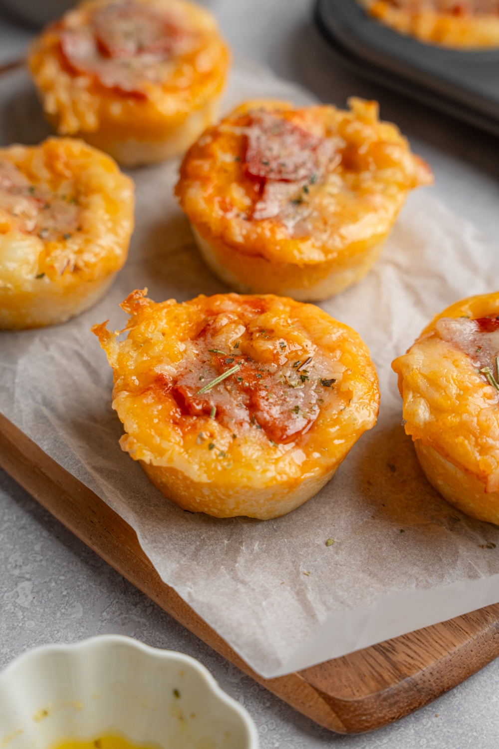 Copycat Little Caesars crazy puffs on a wooden board lined with parchment paper. The puffs are served with extra sauce and herbs on top. The board is on a white counter with a baking tray.
