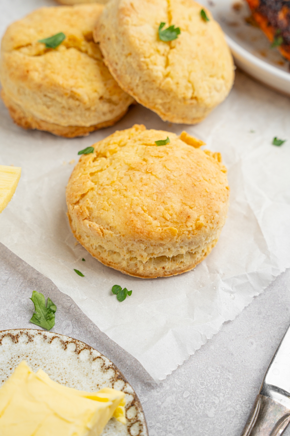 Homemade Popeye's biscuits on a piece of parchment paper garnished with fresh parsley. The parchment is on a white counter with a plate of butter.