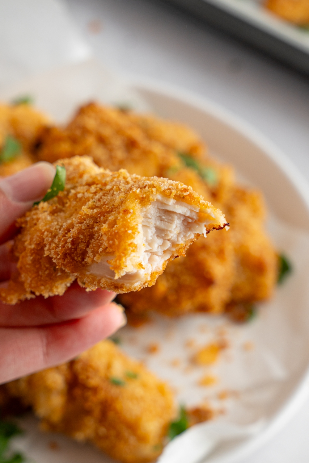 A hand holding a sliced piece of crack chicken. There is a bowl of chicken blurred in the background.