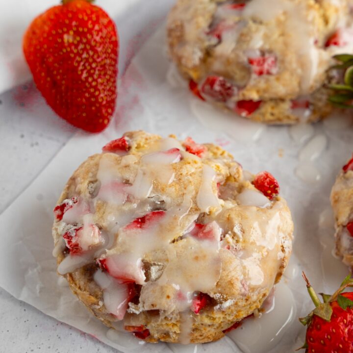 Homemade Popeye's strawberry biscuits on a piece of parchment paper with fresh strawberries. The parchment is on a white counter with a white cloth napkin.