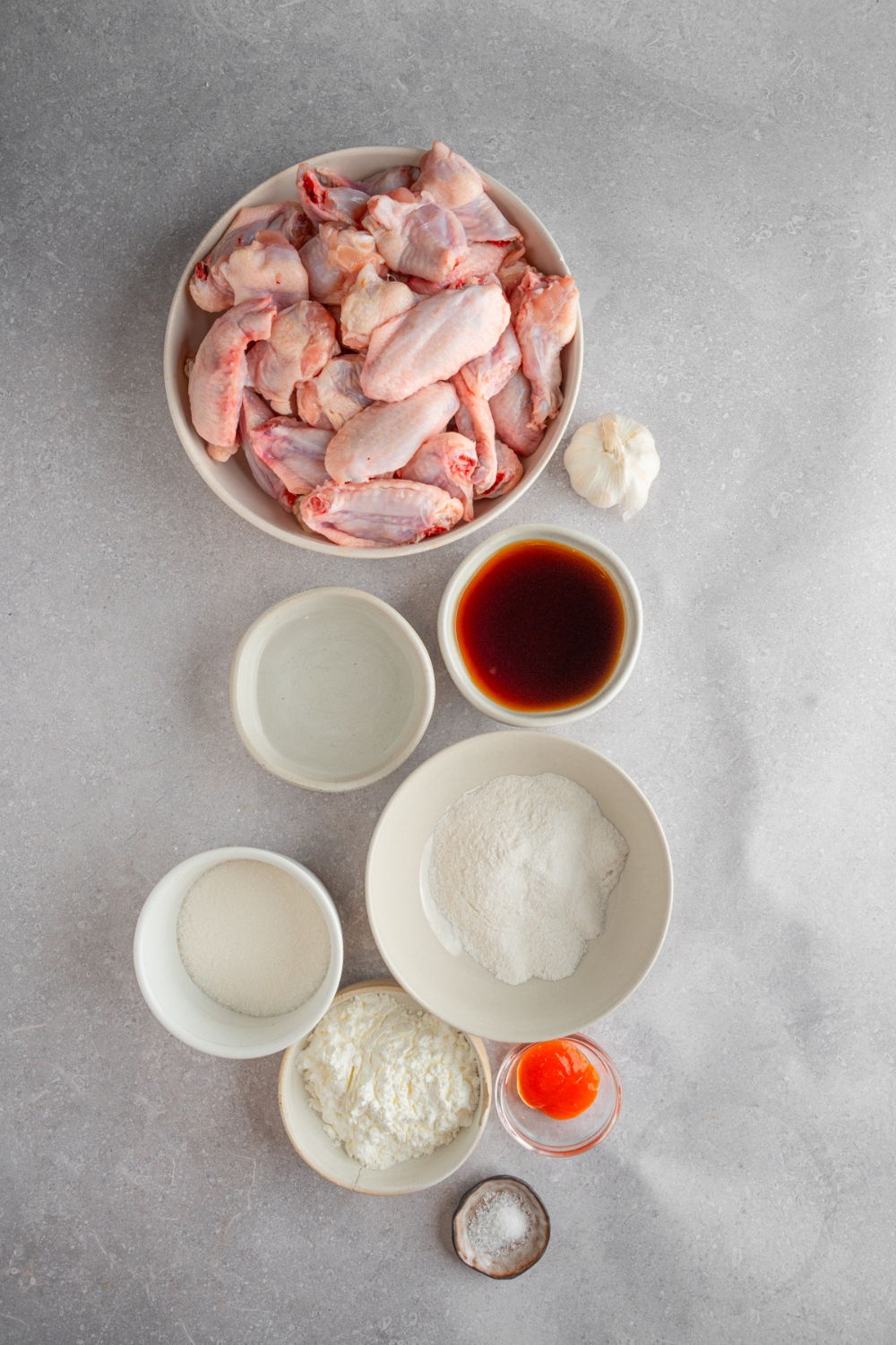 An overhead shot of several bowls in various sizes containing ingredients to make fish sauce chicken wings including uncooked chicken wings, fish sauce, sugar, flour, corn starch, and sriarcha.