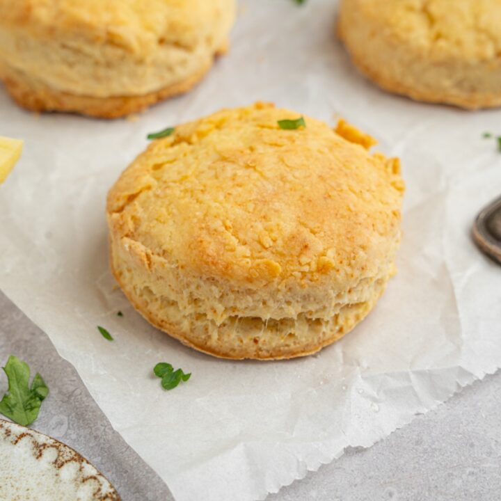 Popeye's biscuits on a piece of parchment paper garnished with fresh parsley. The parchment is on a white counter with a plate of butter.