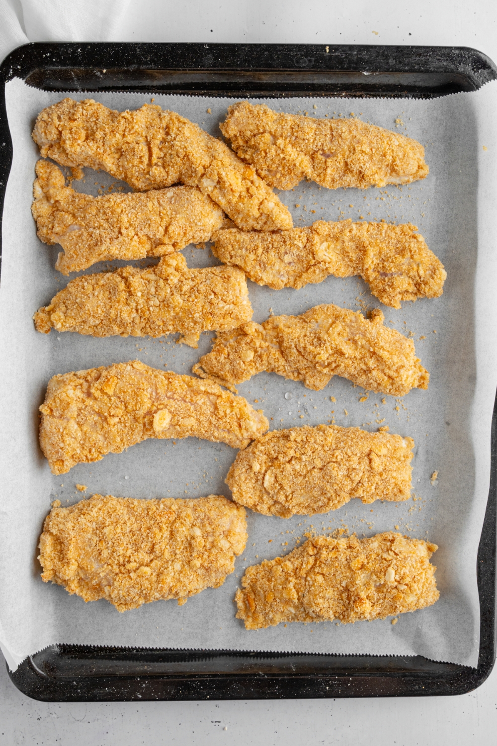 A baking tray lined with parchment paper with several pieces of breaded crack chicken. The tray is on a white counter.