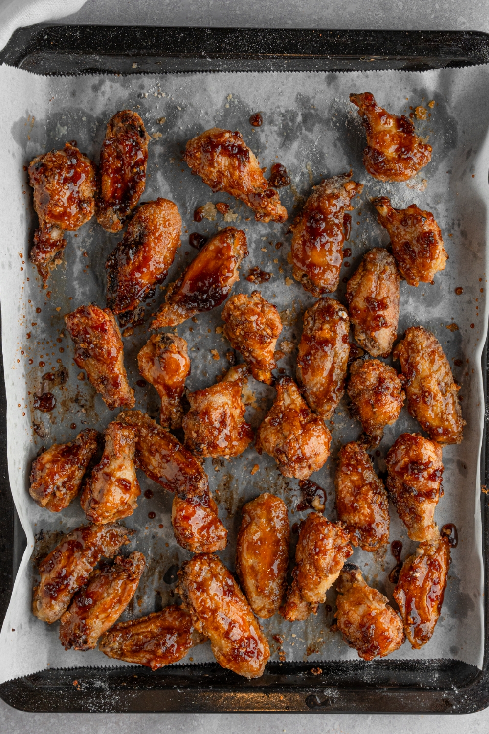 A baking sheet lined with parchment paper with cooked fish sauce chicken wings. The tray is on a white counter.
