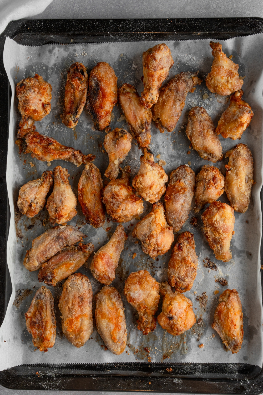 A baking sheet lined with parchment paper with cooked marinated chicken wings. The sheet is on a white counter.