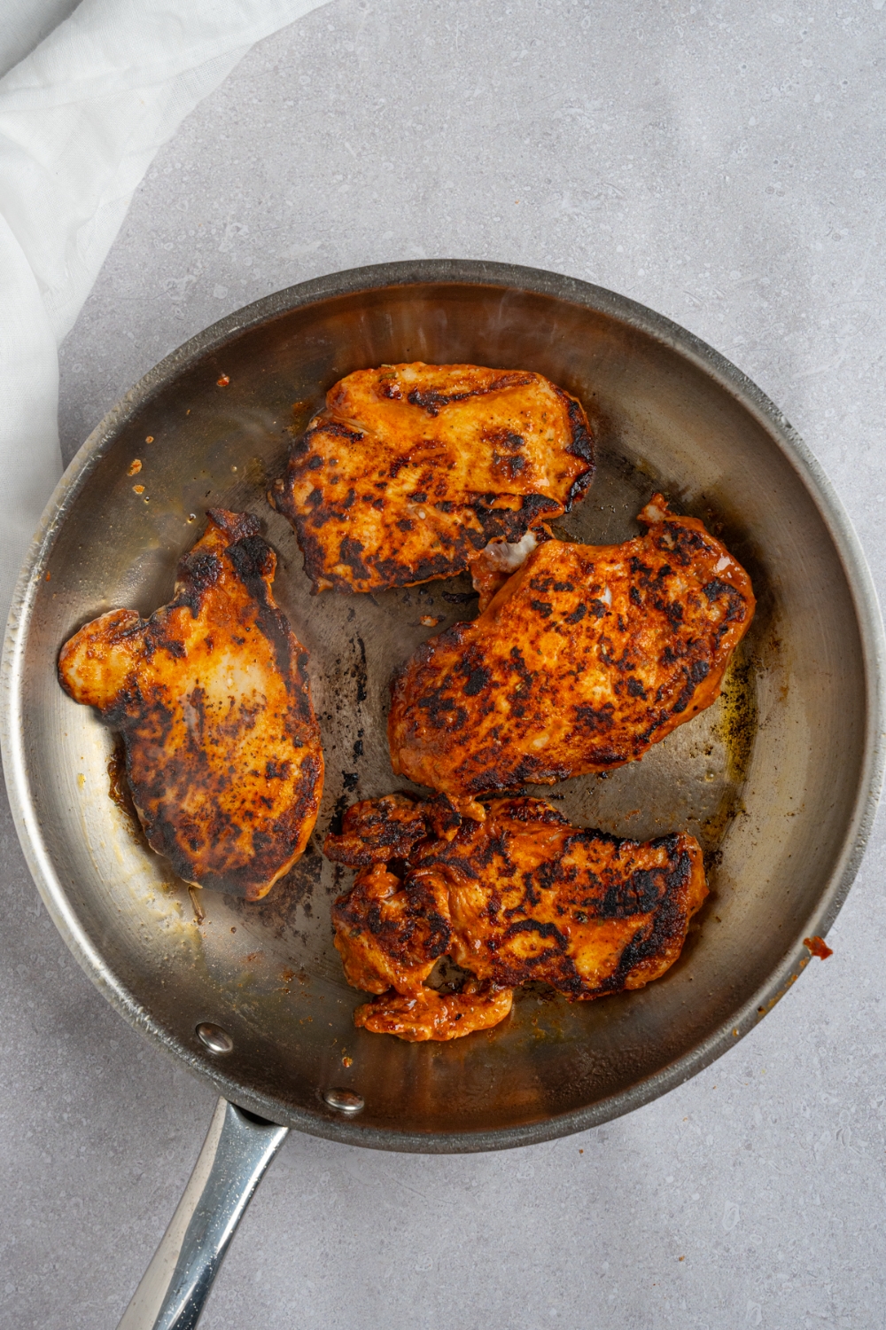 A skillet with four pieces of homemade Popeye's blackened chicken. The skillet is on a white counter.
