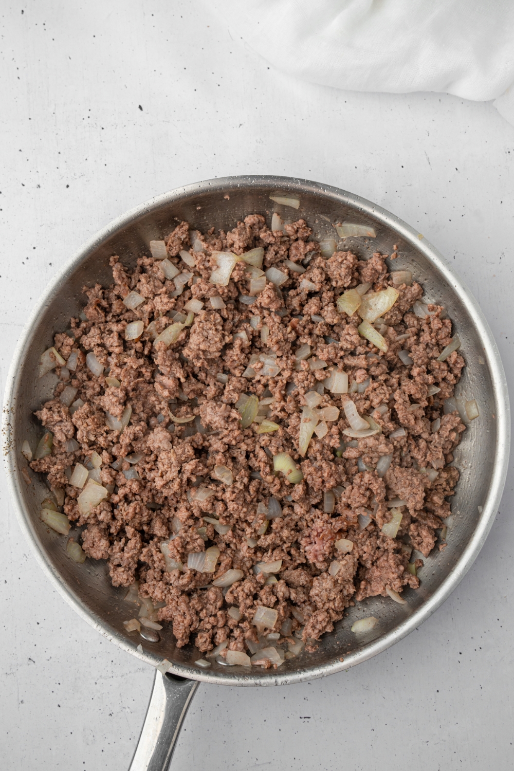A skillet with browned ground beef and onions. The skillet is on a white counter.
