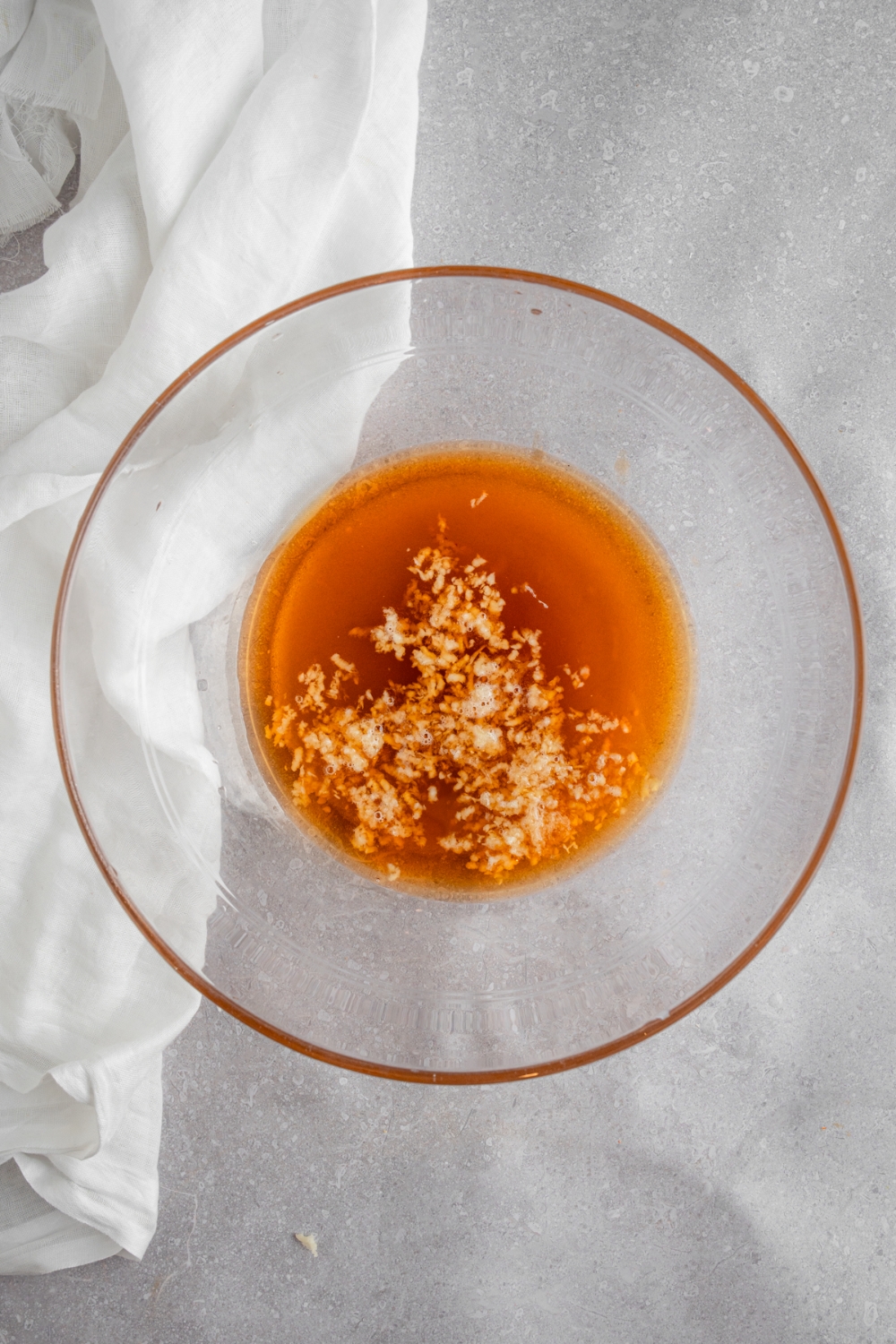 A glass bowl with fish sauce, garlic, water, and salt. The bowl is on a white counter with a white cloth napkin.