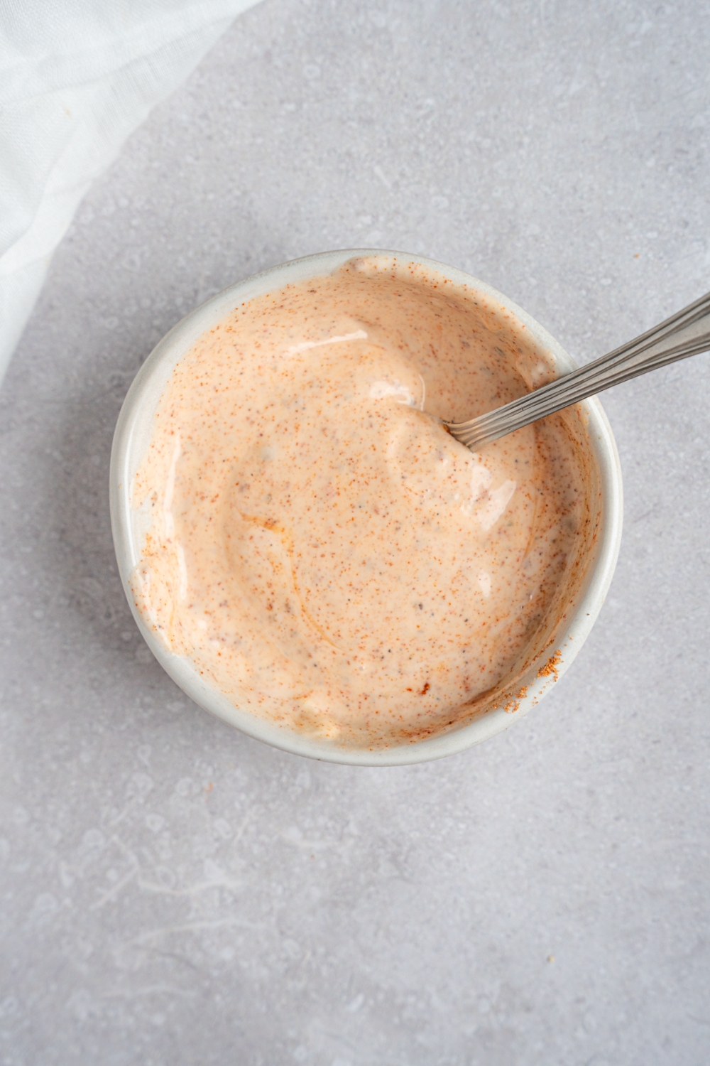 A small bowl with a spoon stirring Popeye's sauce. The bowl is on a white counter.