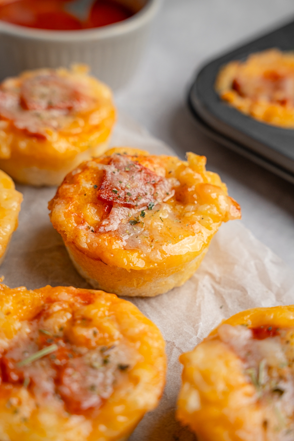 Copycat Little Caesars crazy puffs on a wooden board lined with parchment paper. The puffs are served with extra sauce and herbs on top. The board is on a white counter with a baking tray.