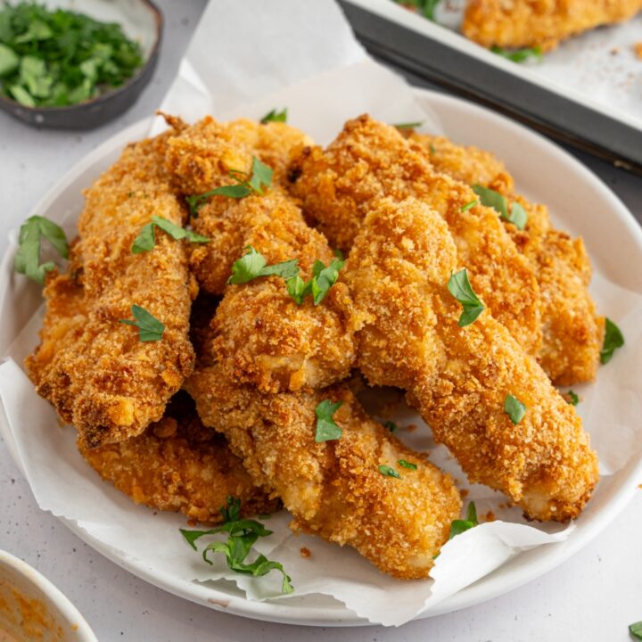 Crack chicken garnished with fresh parsley served in a bowl lined with parchment paper. The bowl is on a white counter with a tray of chicken and small ramekin of garnishes and bowl of dipping sauce.